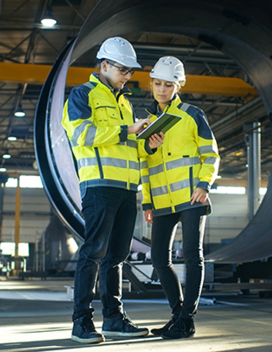 Two engineers in high visibilty jackets and hard hats looking at clipboard